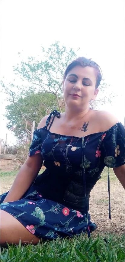 Vera Donizete Braz sentada na grama em um cenário rural